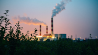 Factory with chimney flues and smoke with plants in foreground